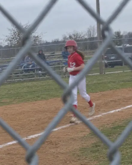 A blurry phone photo of a girl in a red uniform, seen through a chain-link fence